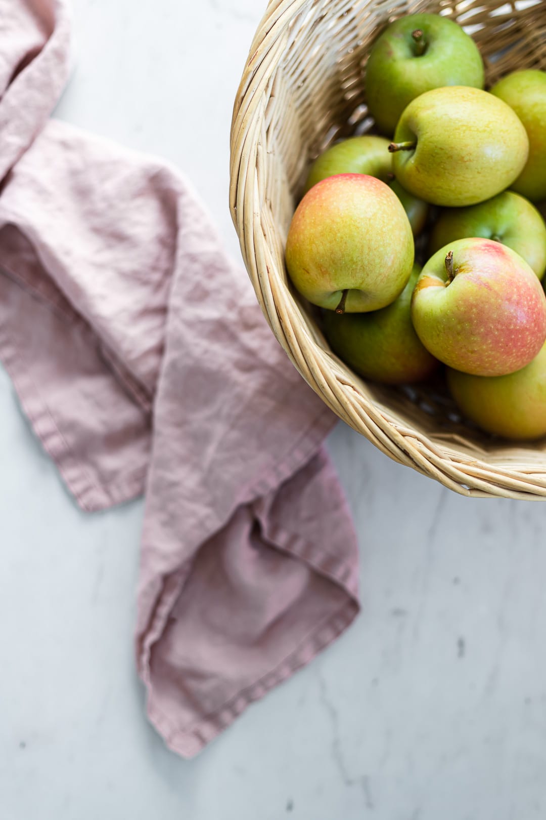 Green apples in a basket on a white marble background with pink linen nearby