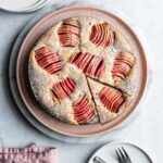 Cake with apples with a slice cut out, on a white marble background and white plates nearby