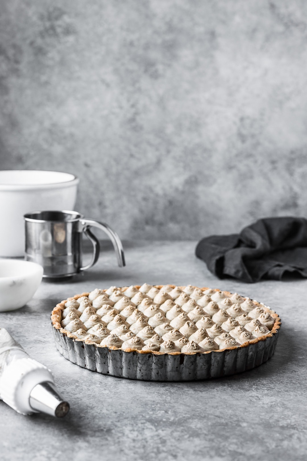 Tart resting on a grey background with bowls and piping bag nearby