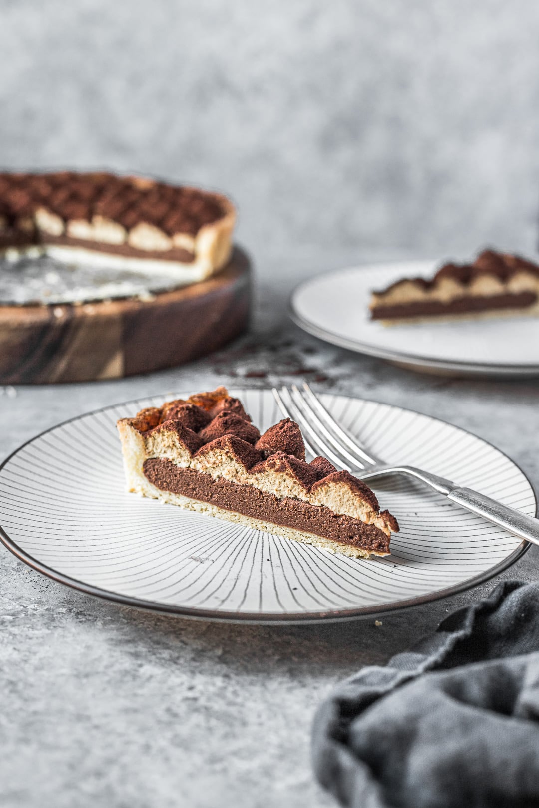 Slice of tart on plate on a grey background with rest of tart in background