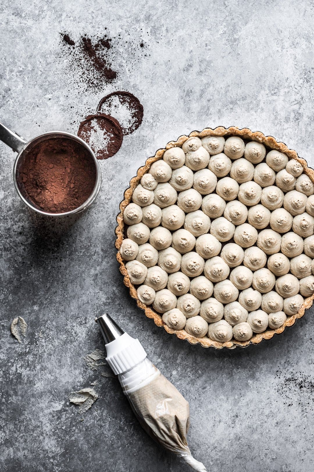 Chocolate coffee mascarpone tart on a grey background with cocoa powder and piping bag nearby