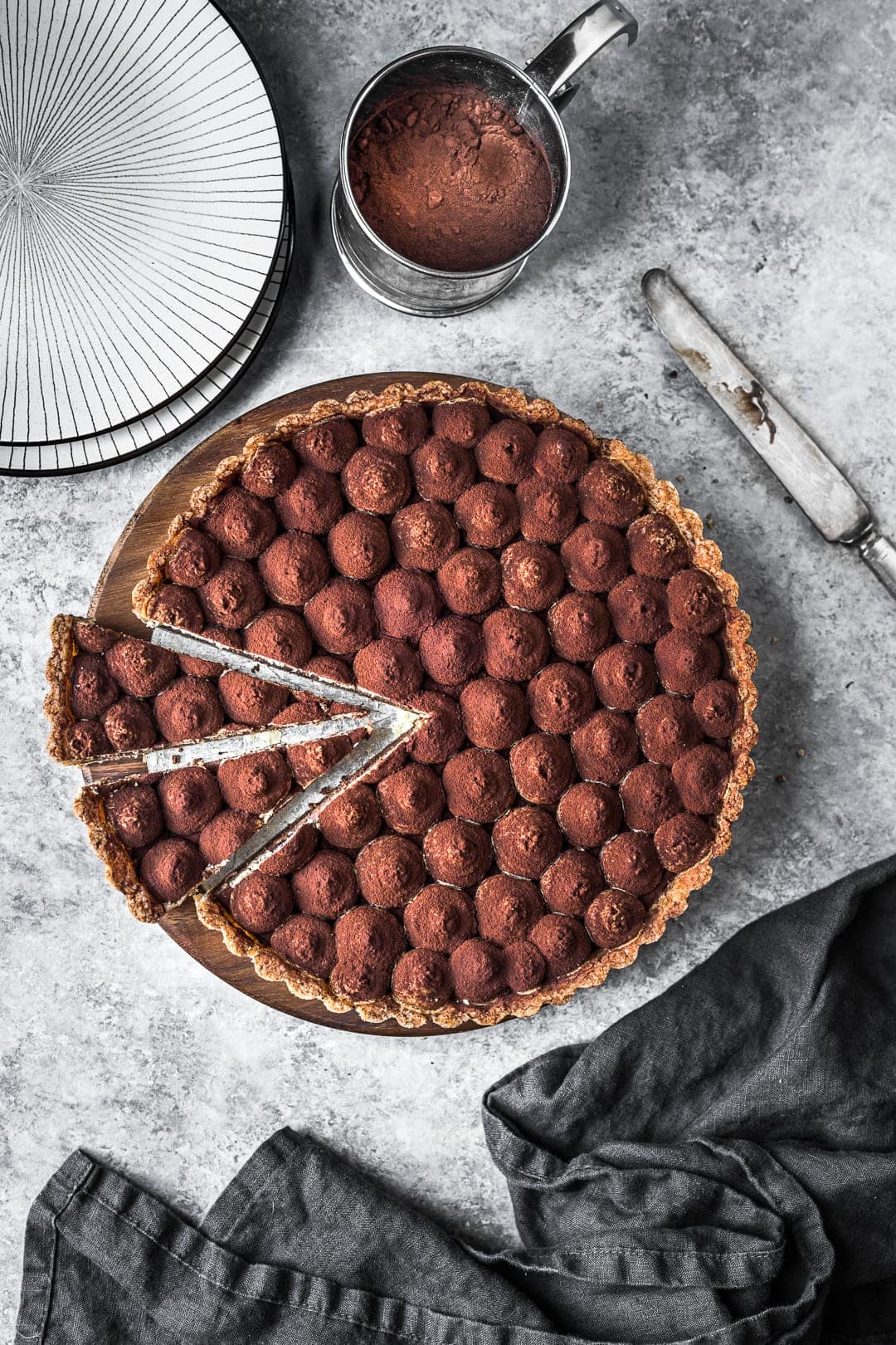 Tart with two slices cut, on a grey background with napkin and plates nearby