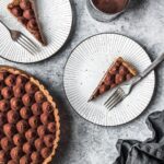 Two slices of tart on plates with rest of tart and sifter of cocoa powder nearby