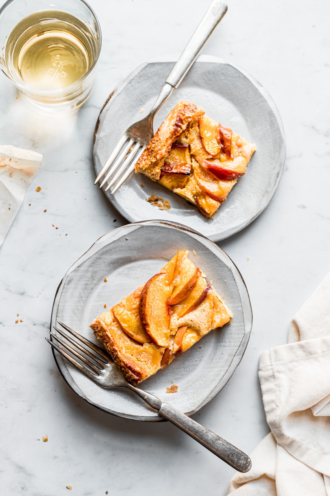 Slices of peach galette on ceramic plates and a marble background with a glass of white wine nearby