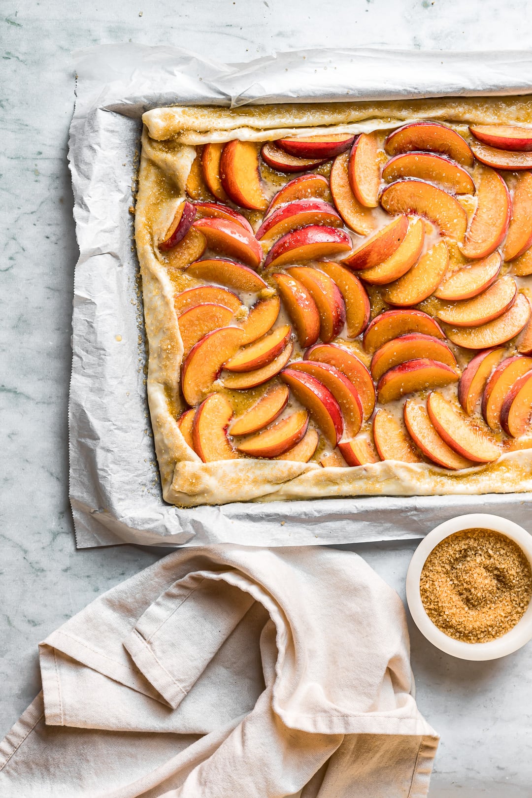 Closeup of unbaked peach galette on parchment and a white marble background