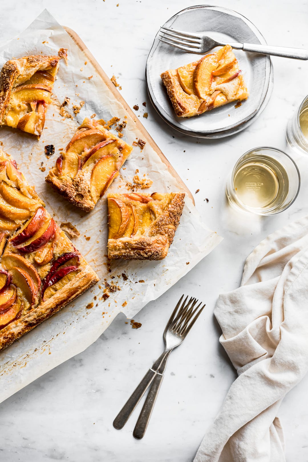 Peach galette slices on a parchment covered cutting board with plates and forks nearby