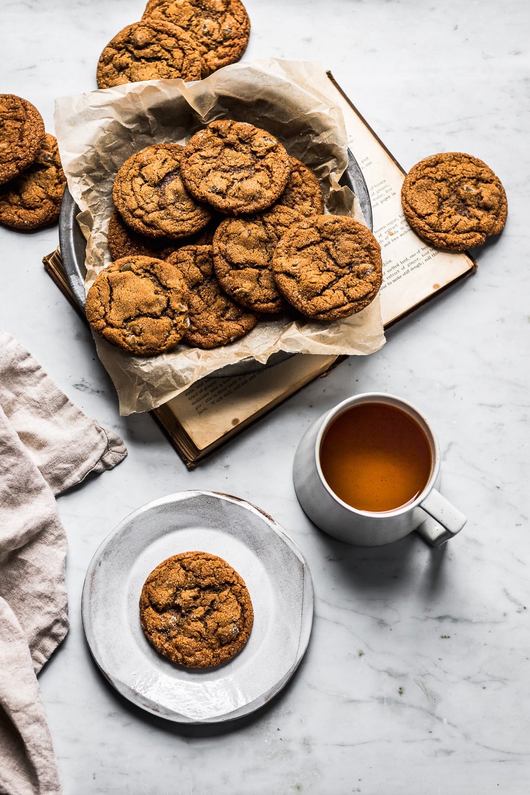 Table scene of ginger molasses cookies in container with book, plate and tea nearby