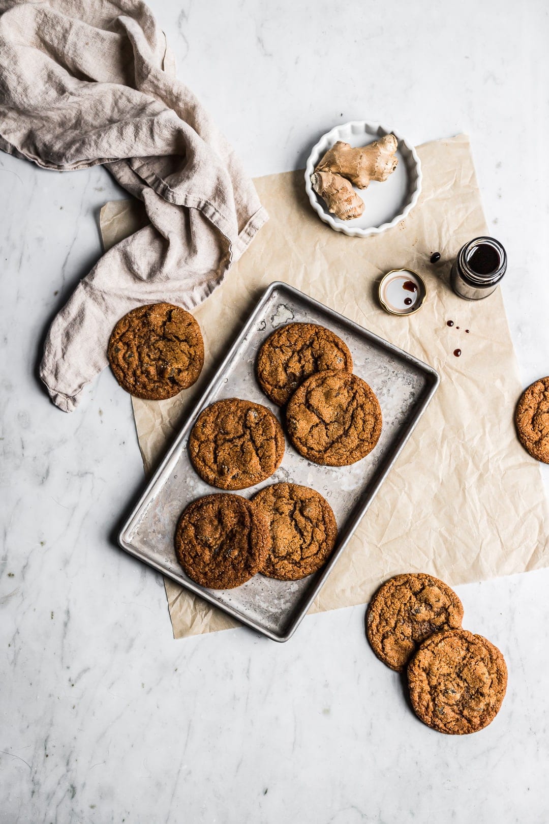 Cookies on pan with ginger and molasses nearby - all on a white marble background