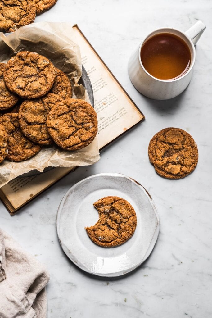 Cookies on a dish with a book, tea and plate nearby.
