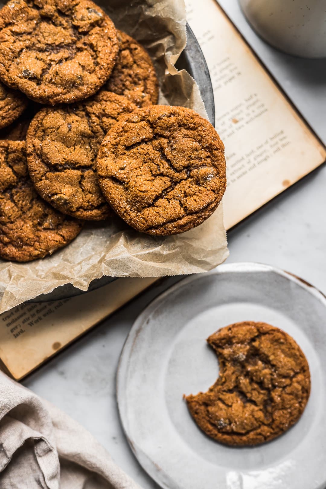 Close up of ginger molasses cookies in a pan with a cookie nearby on a plate with a bite taken out of it