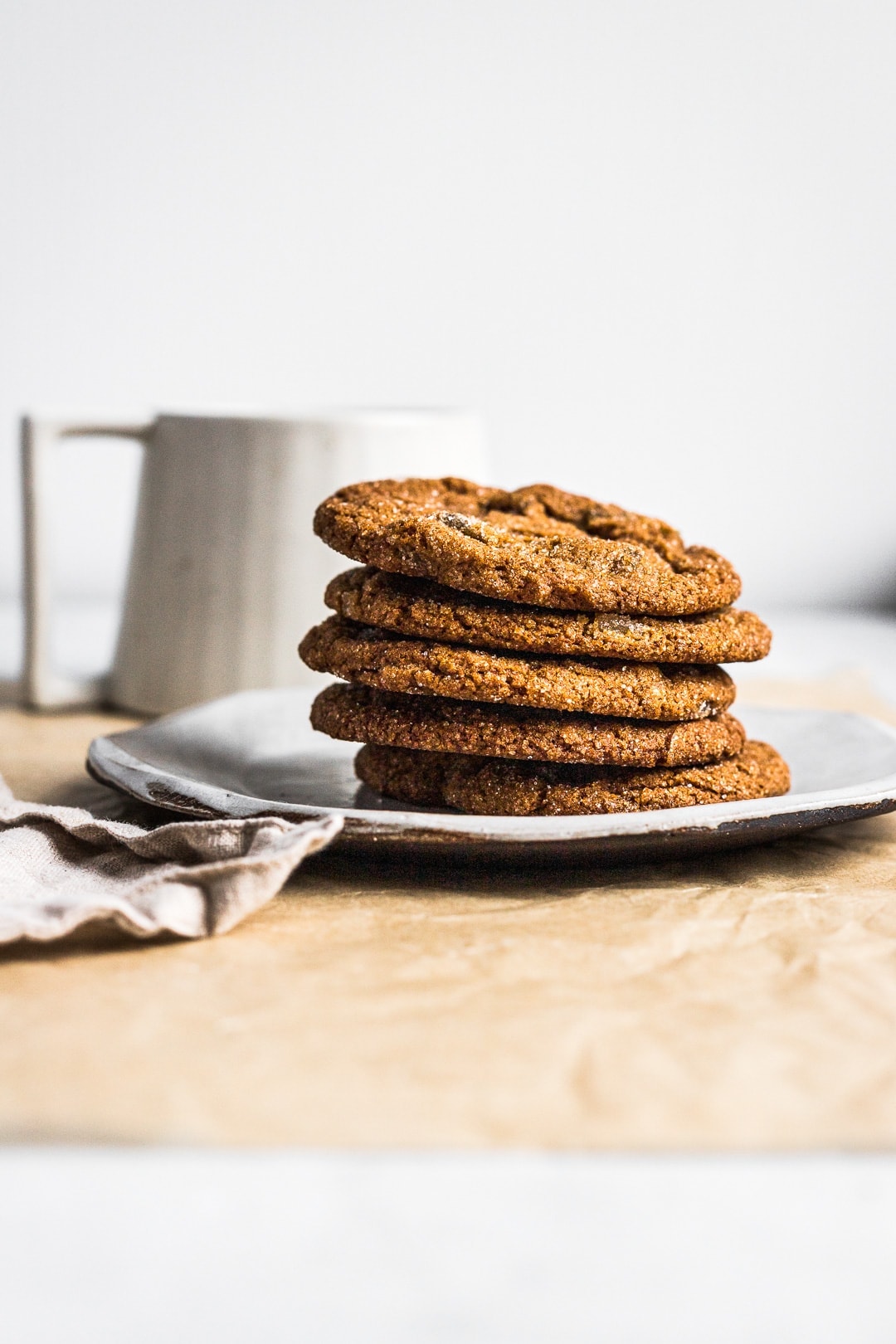 Side view of 5 ginger molasses cookies stacked on a plate with a cup of tea in background