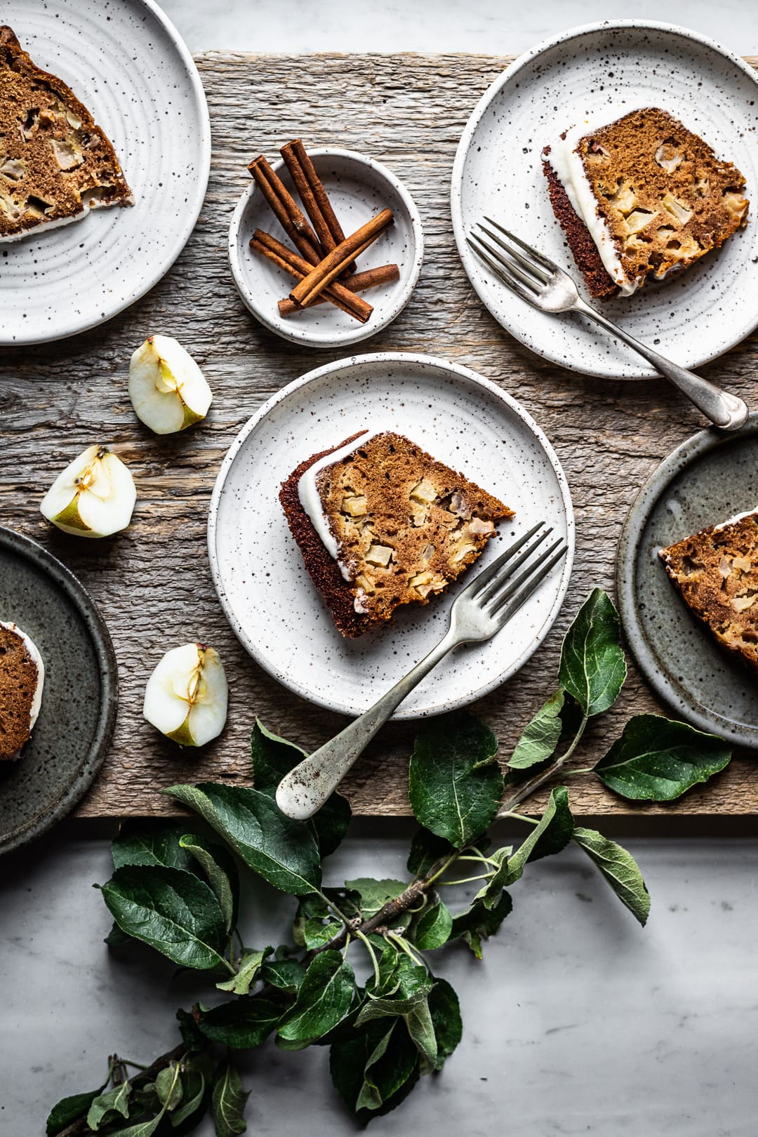 Slices of apple bundt cake on plates with forks, cinnamon sticks and apple slices as decoration