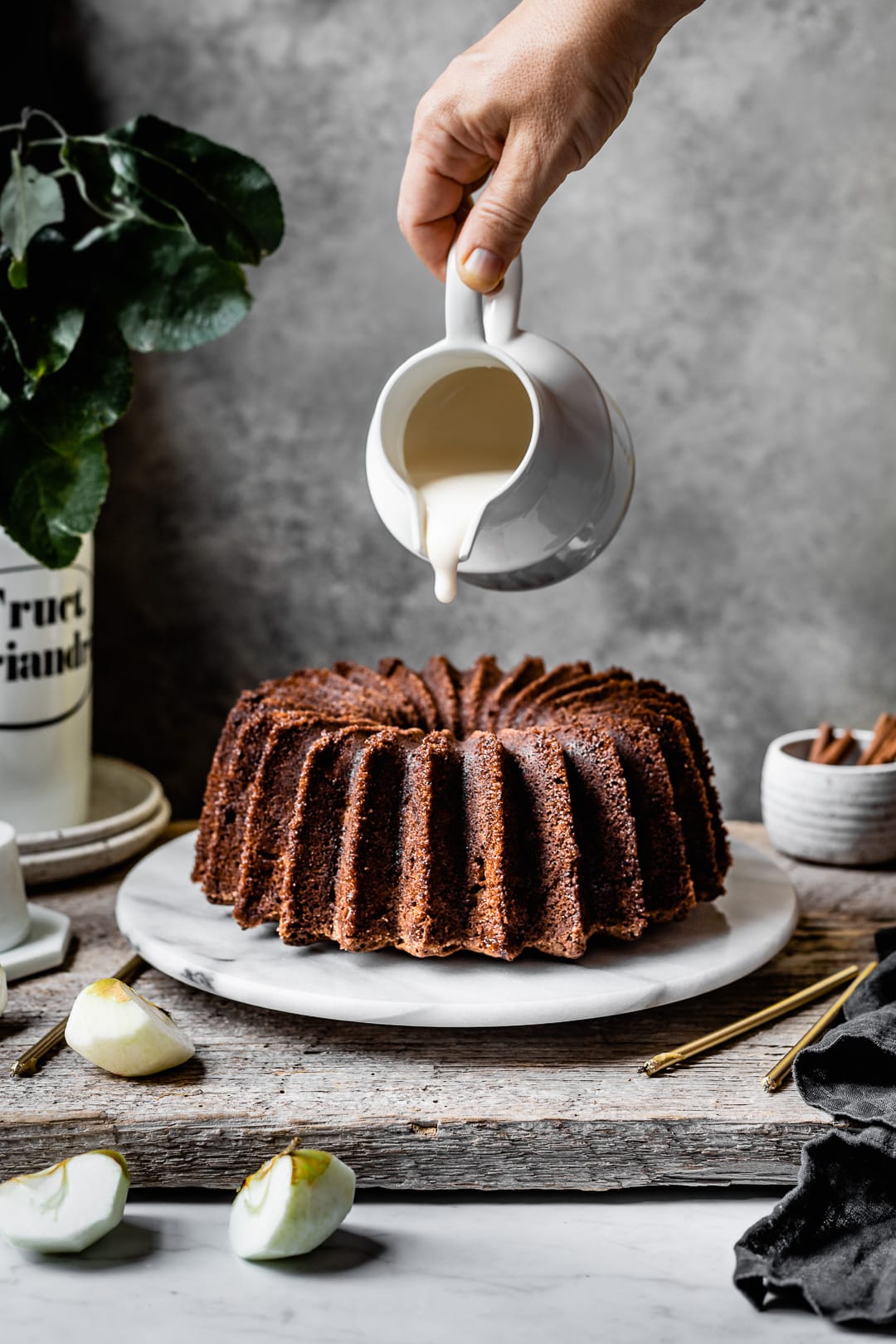 Hand pouring white glaze onto an apple bundt cake