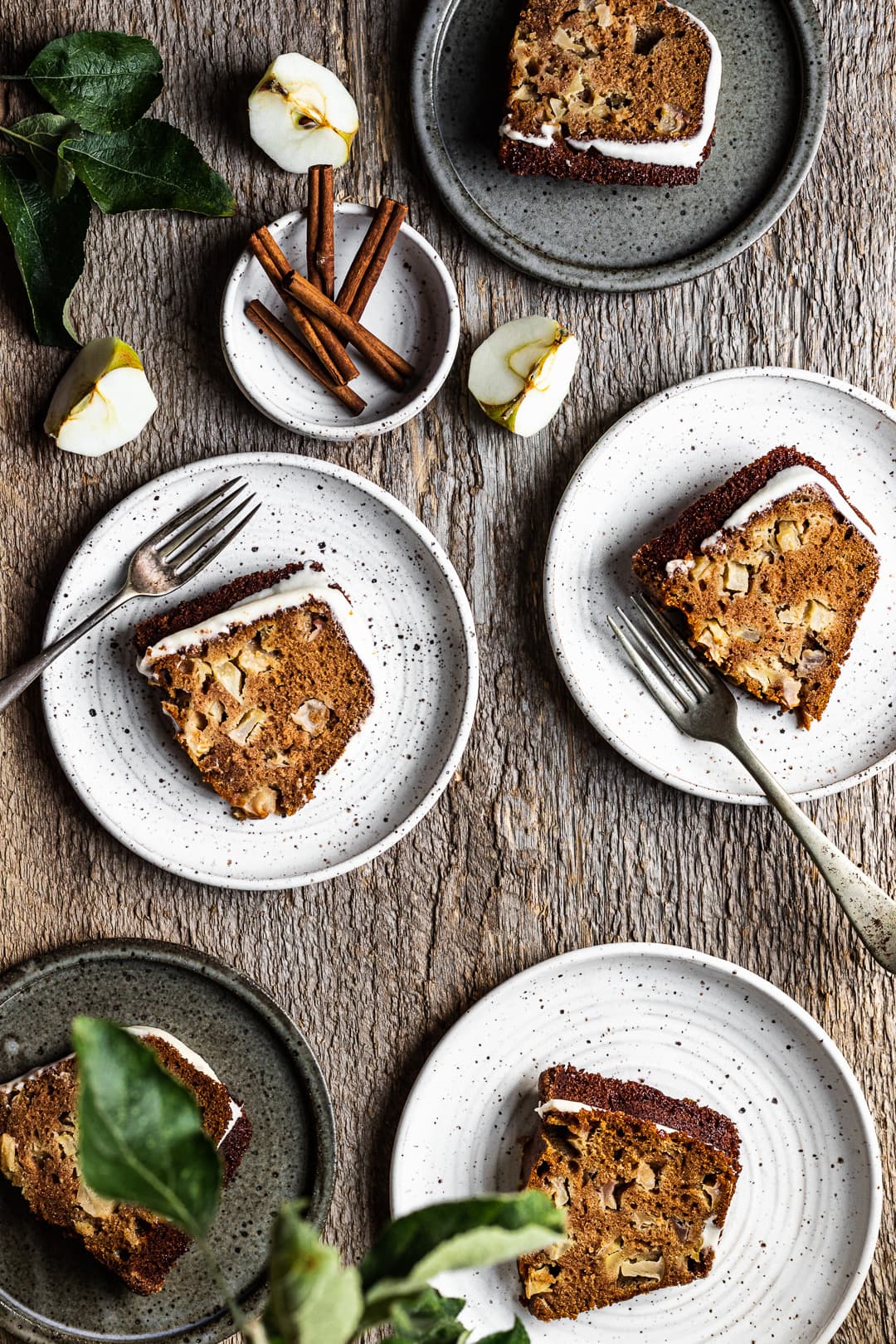 Slices of bundt cake on ceramic plates with forks, cinnamon sticks and apple slices as decoration