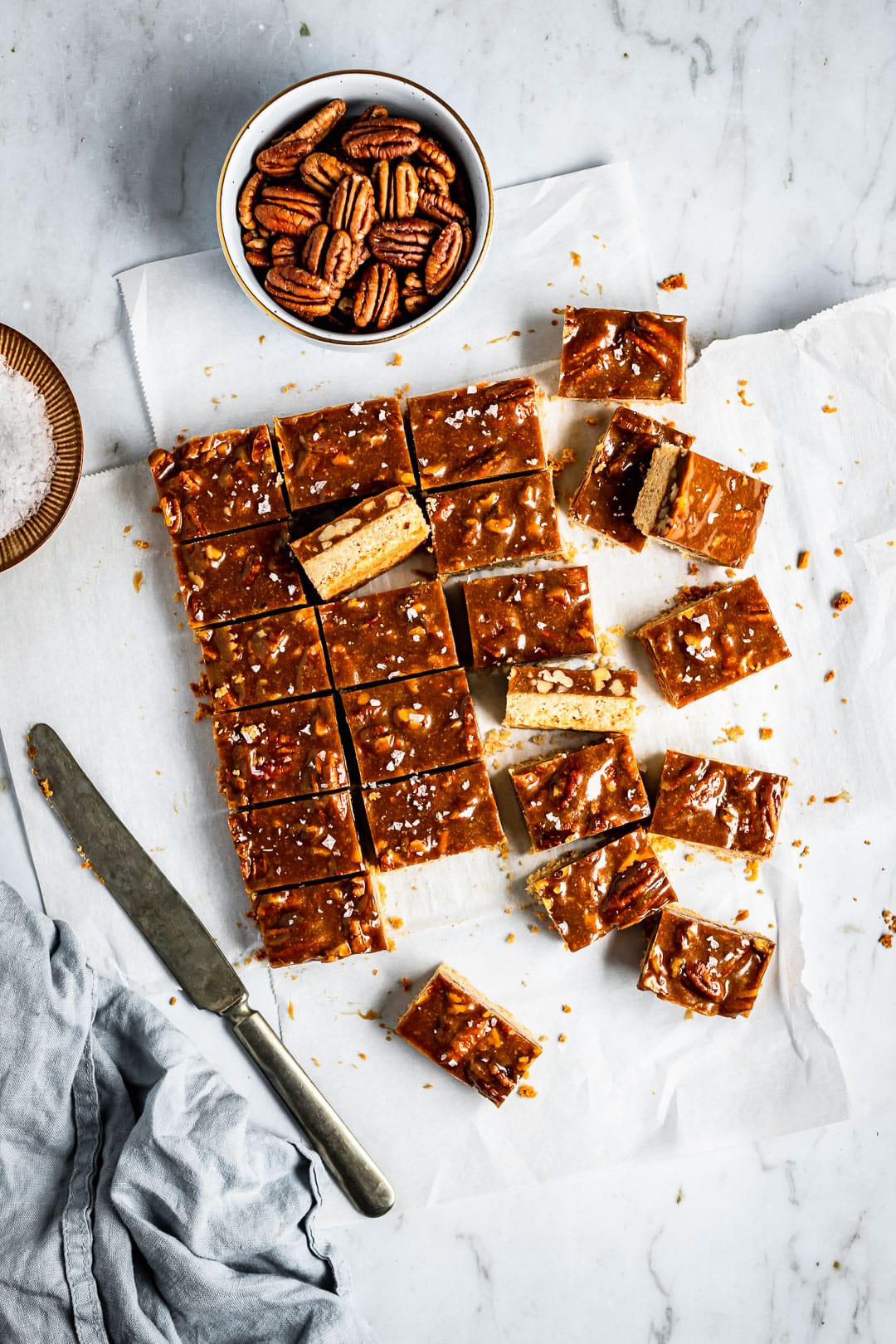 Sliced honey caramel pecan bars on parchment paper and a marble surface