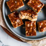 Honey caramel pecan shortbread bars on a blue plate with a bite taken out of one