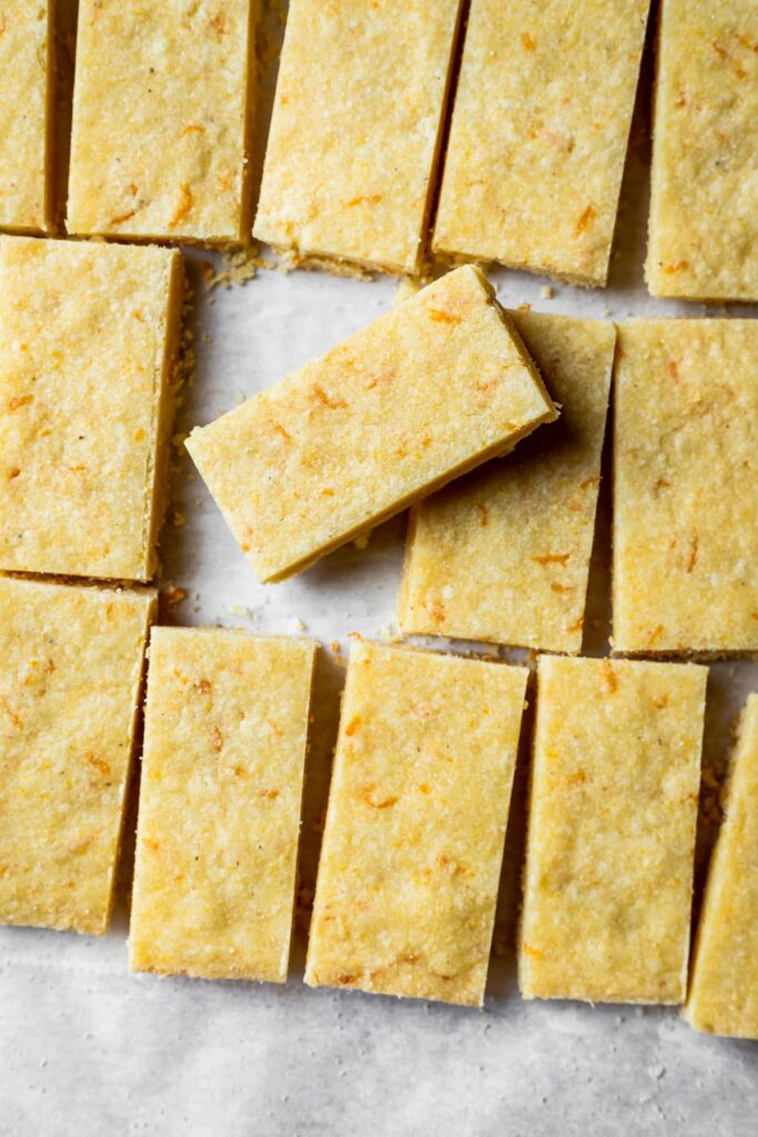 Shortbread cookies with orange zest cut into rectangles on white parchment paper.