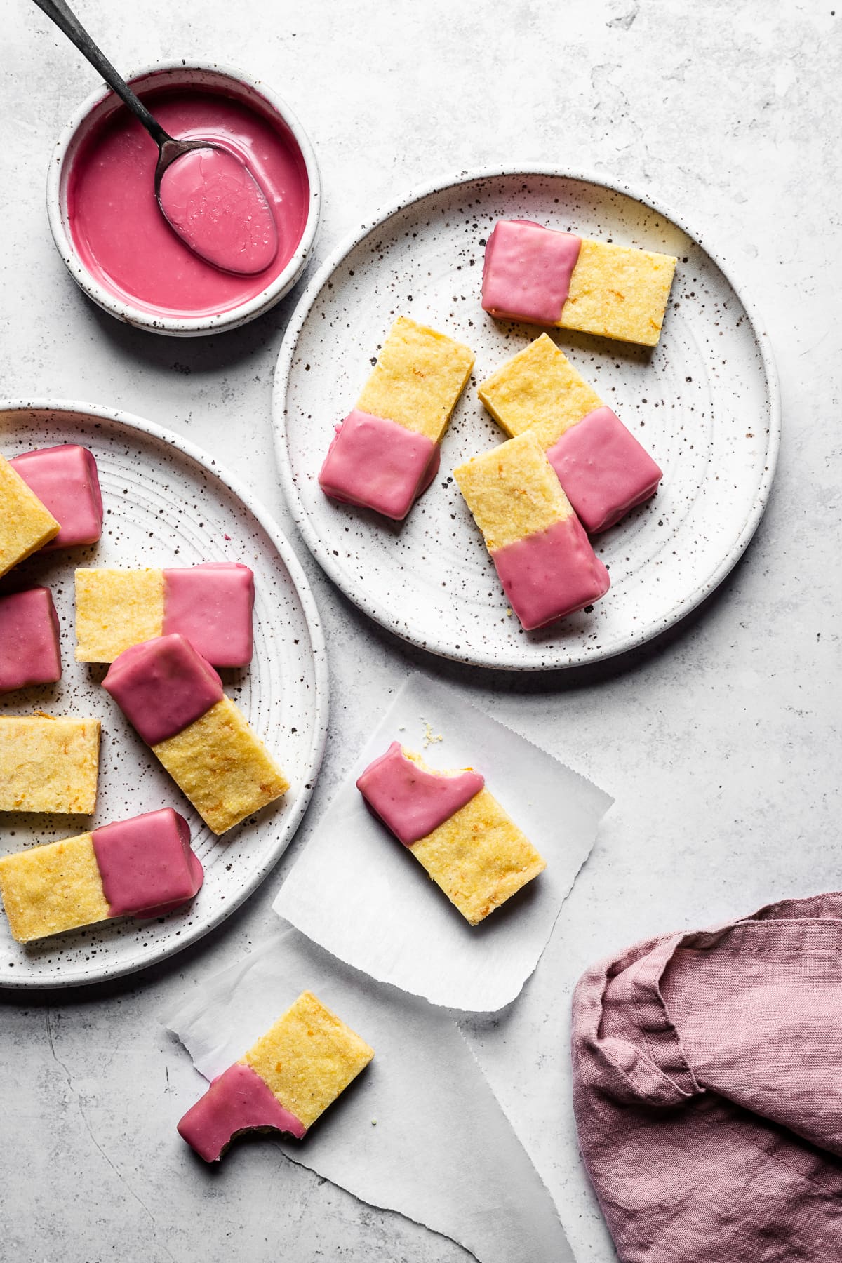 Cornmeal shortbread bars dipped in pink blood orange glaze on white plates and white parchment squares