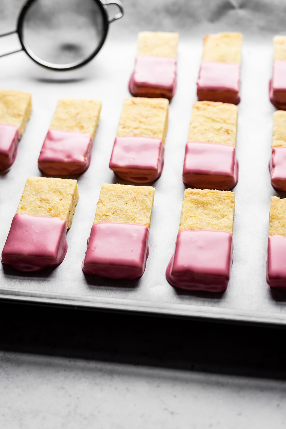 Shortbread cookies dipped in pink glaze drying on a parchment lined cookie sheet