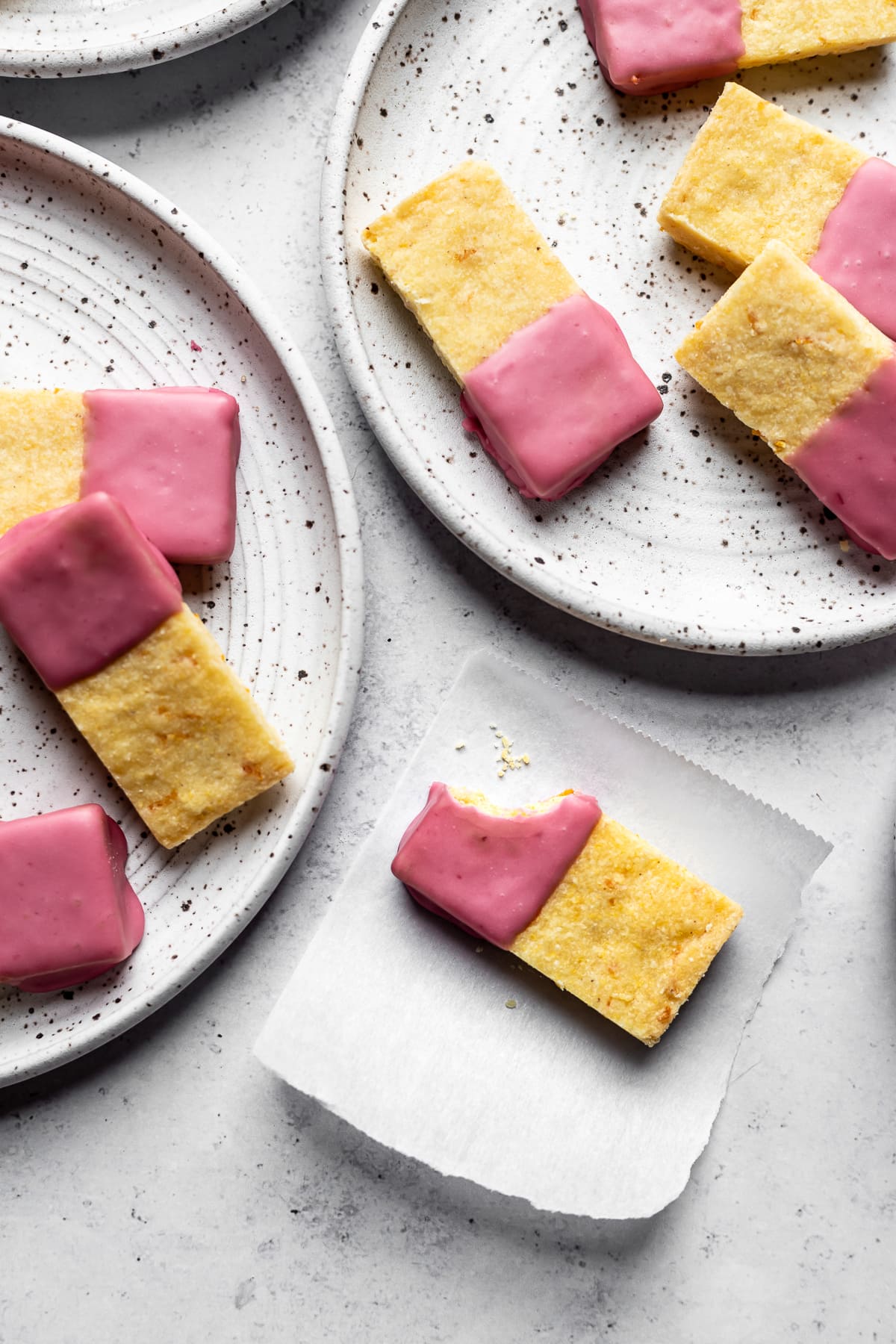 Glazed shortbread bars on white speckled plates with a bite taken out of one bar