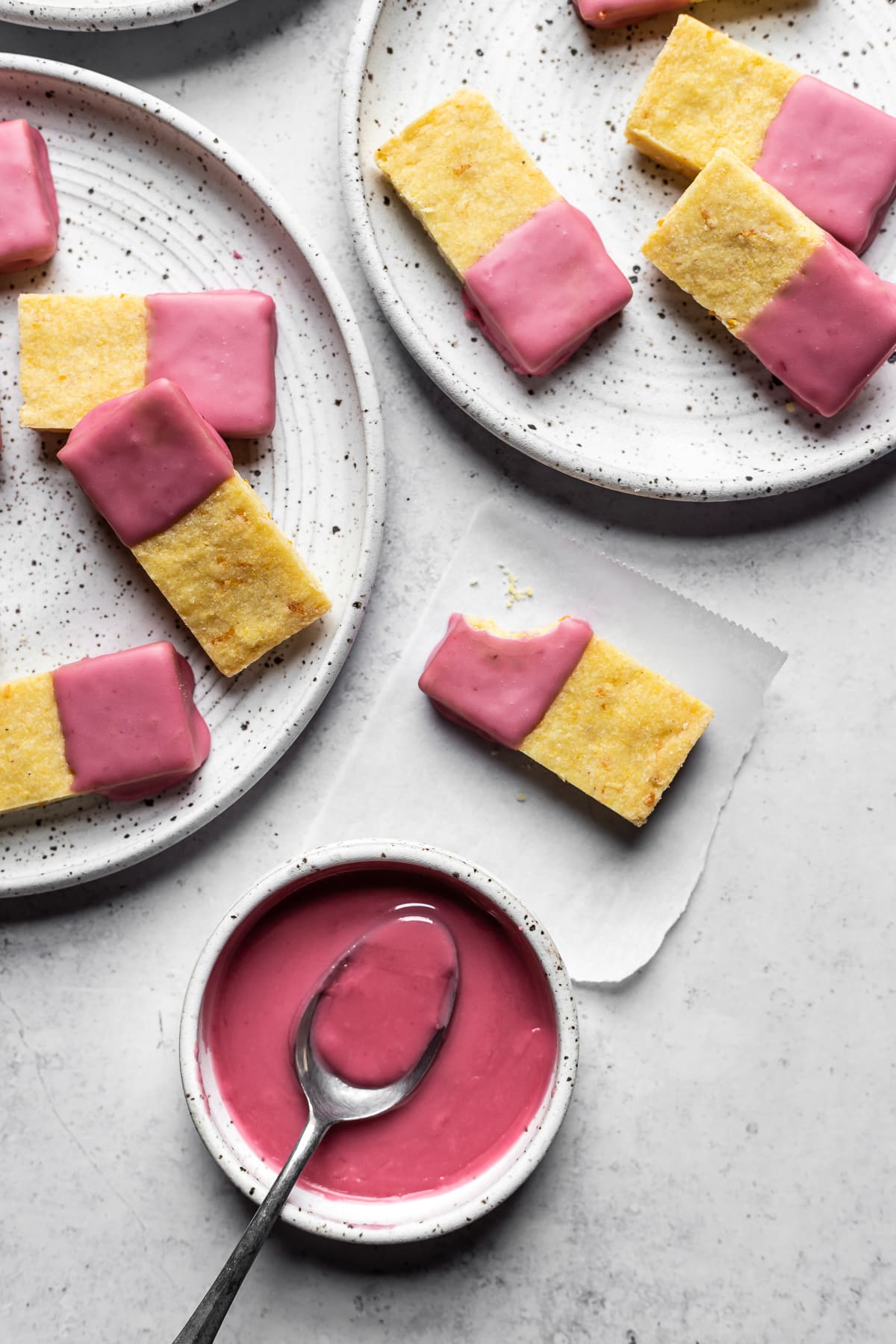 Shortbread cookies with pink glaze on white speckled plates and a white background