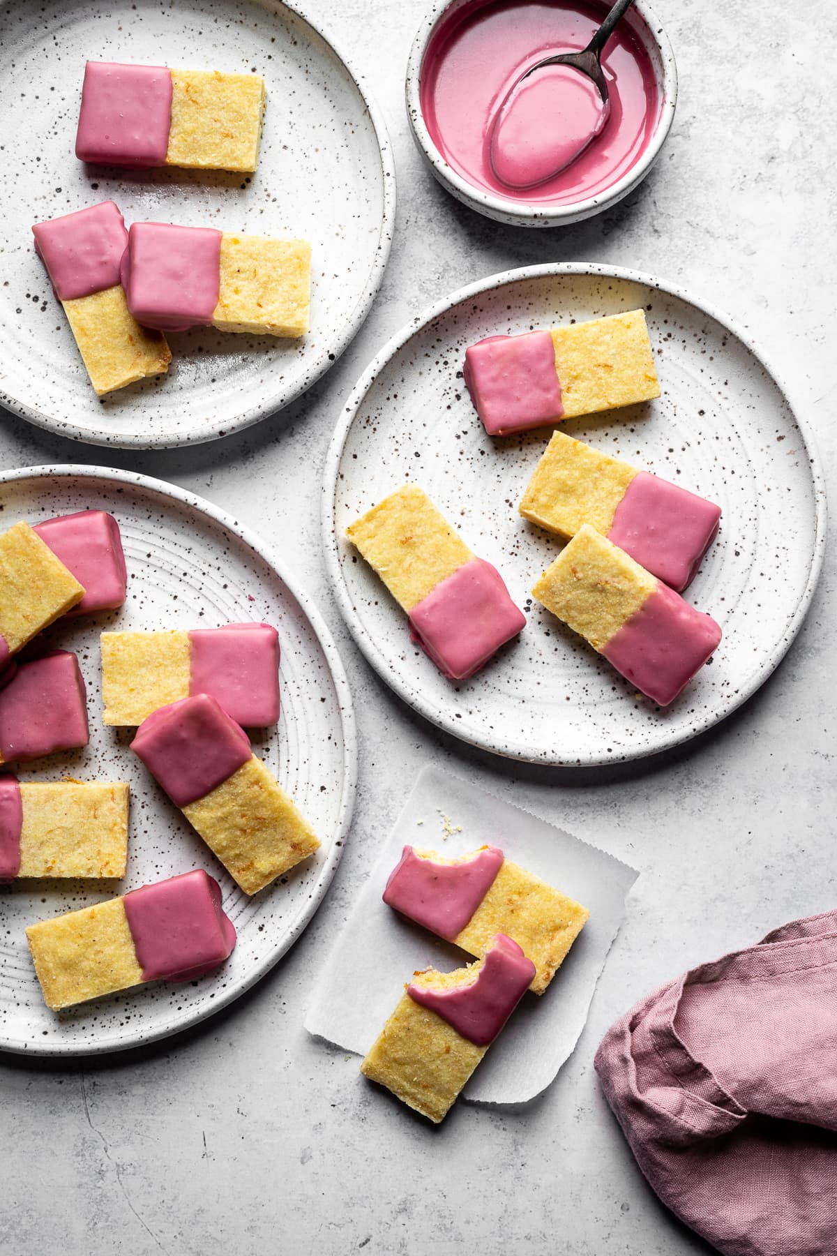 Shortbread cookies dipped in pink blood orange glaze on white plates and a white background