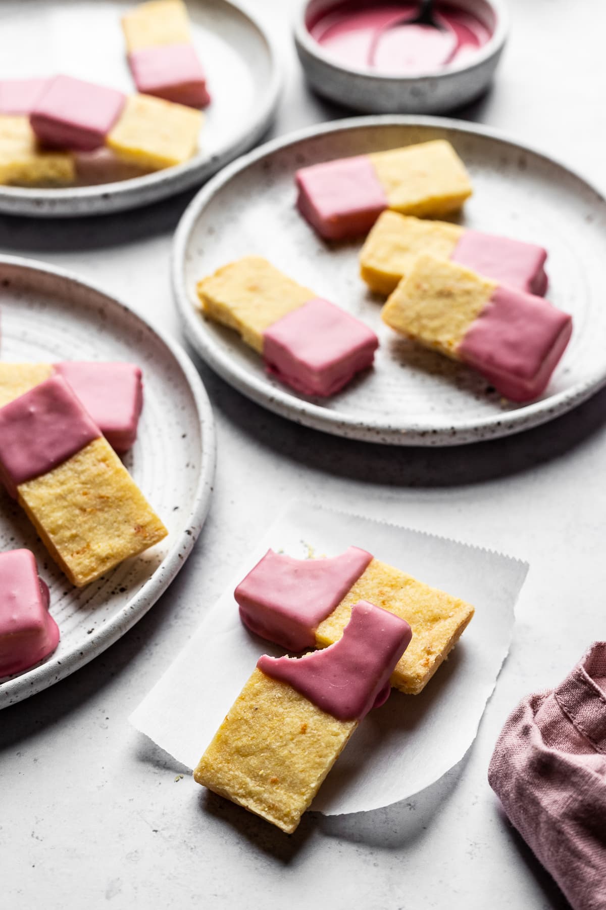 Angled photo of cornmeal shortbread bars dipped in pink glaze on white plates and white background