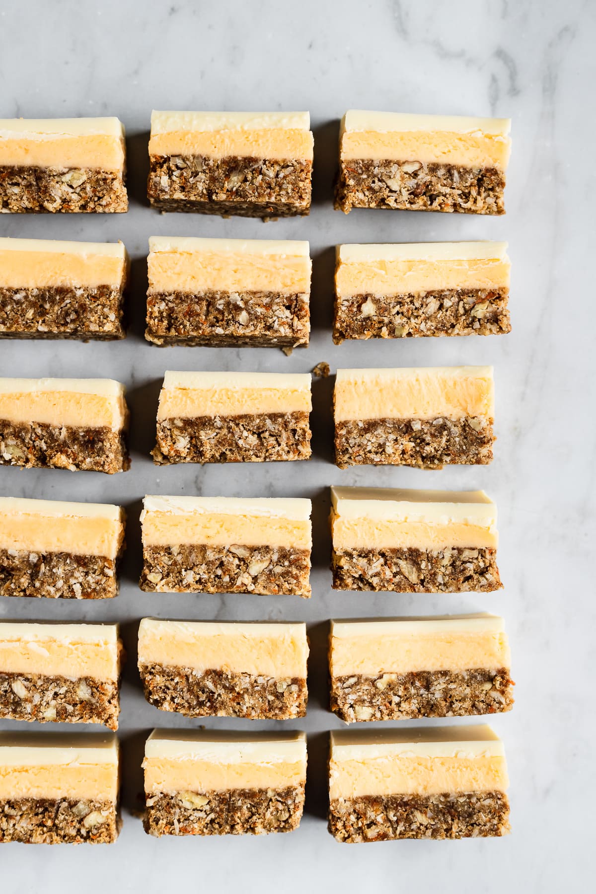 Three rows of sliced bar cookies on a white marble background turned on their side to show the layers