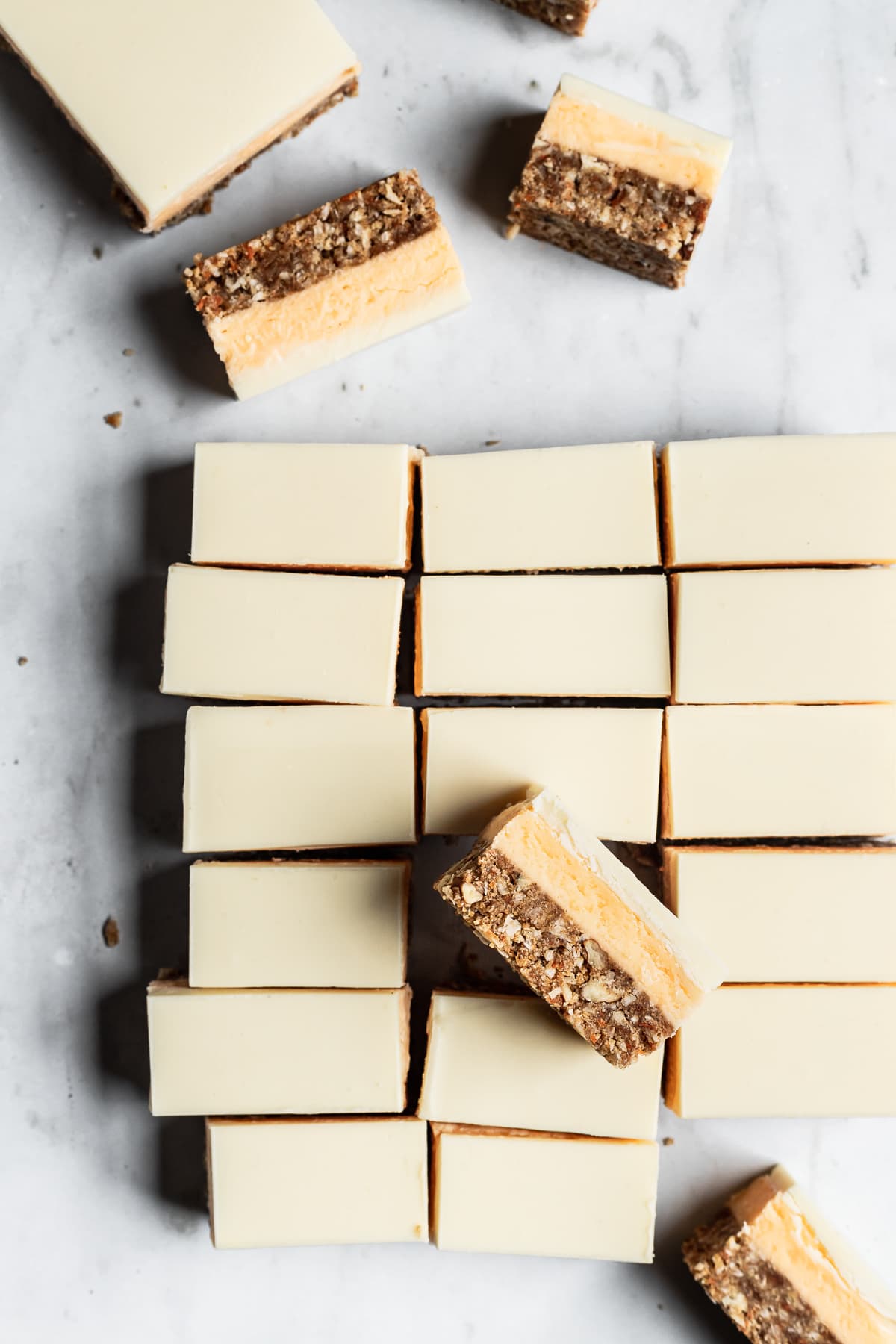 A grouping of bar cookies on a white marble background cut into slices with some turned on their side to show the layers