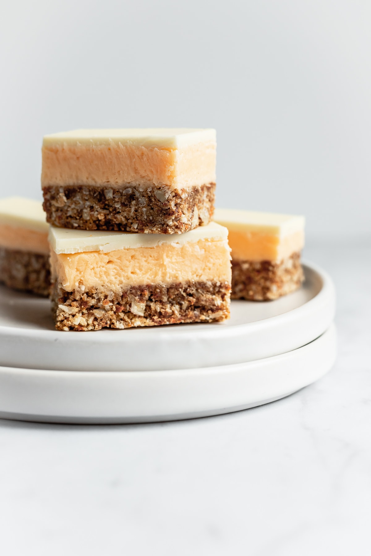 Sliced carrot cake bar cookies stacked up on a white plate and a white marble background