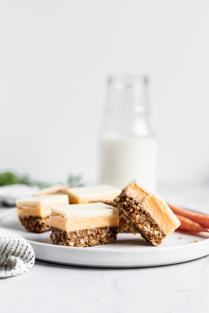 Sliced carrot cake bars on a white plate with a glass milk bottle in the background