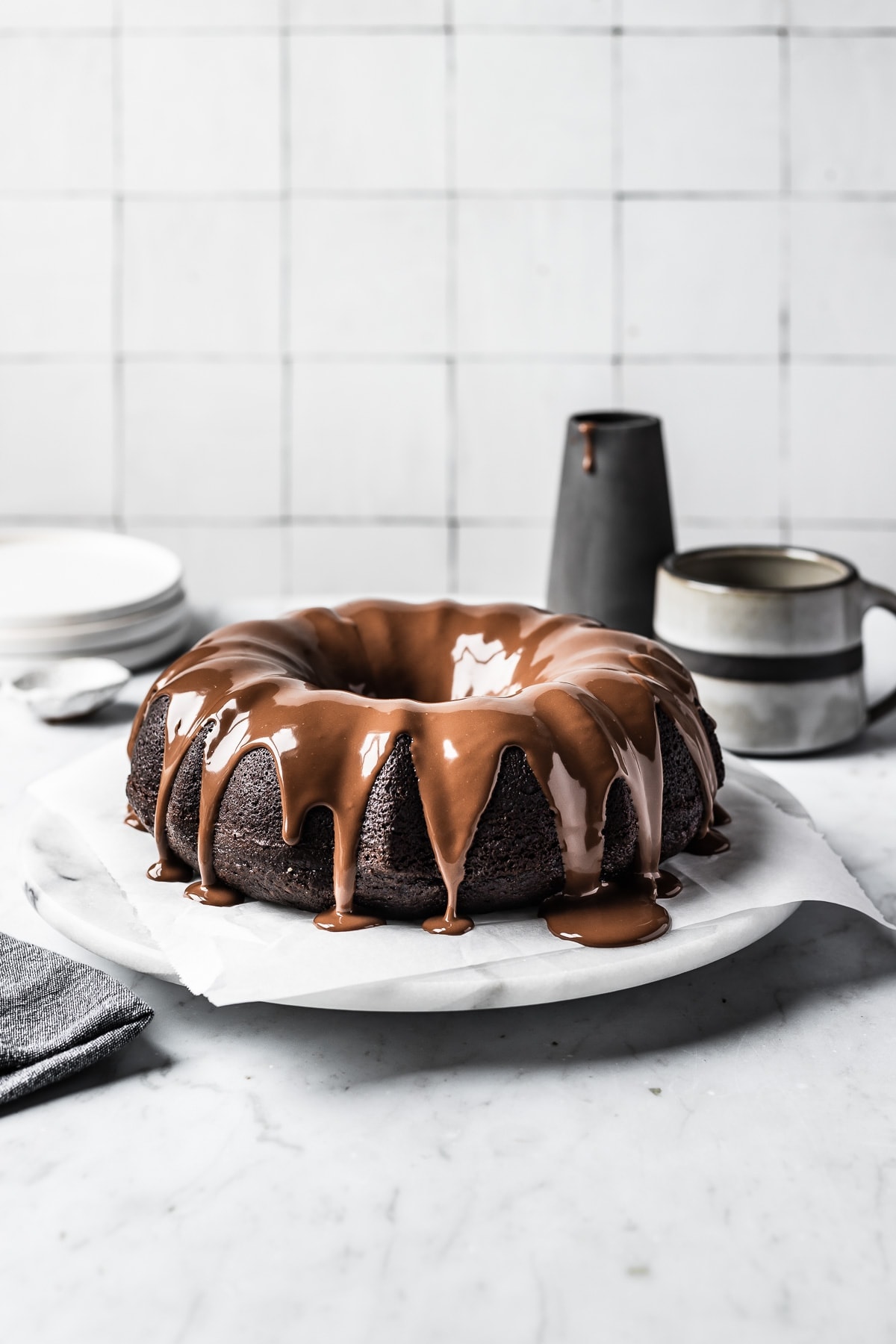 A chocolate cake drizzled with a chocolate ganache on a marble platter and marble countertop