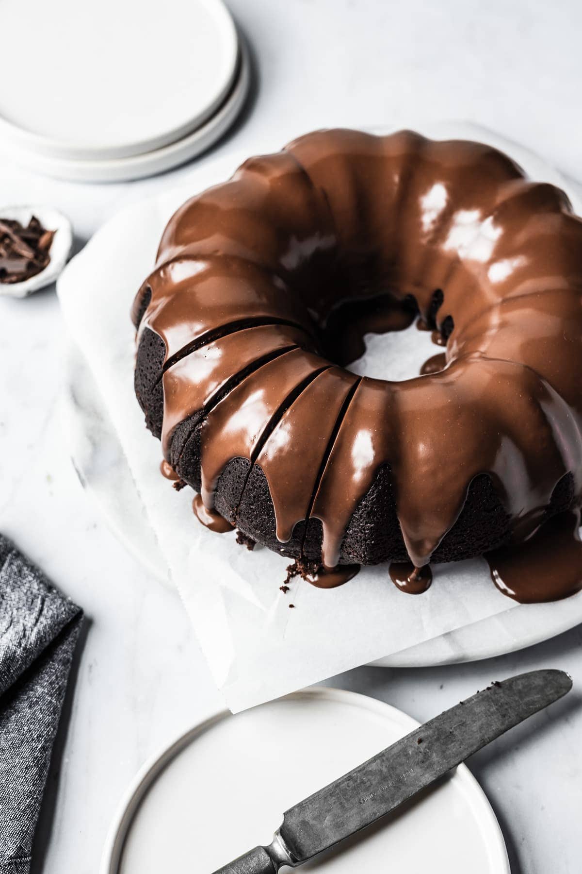 Close up of sliced chocolate olive oil bundt cake with chocolate ganache glaze on a white marble platter