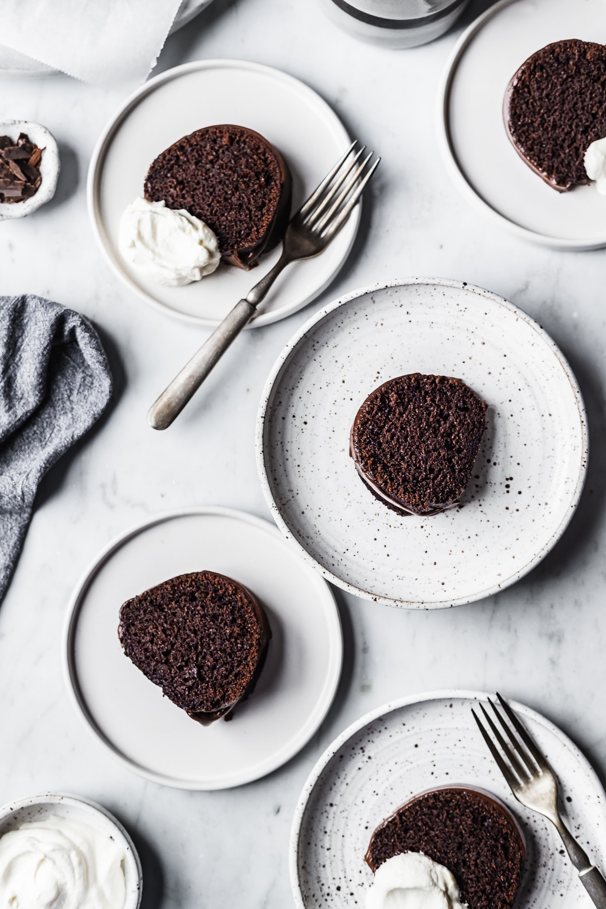 Five white plate each with a slice of chocolate bundt cake resting on a marble surface 