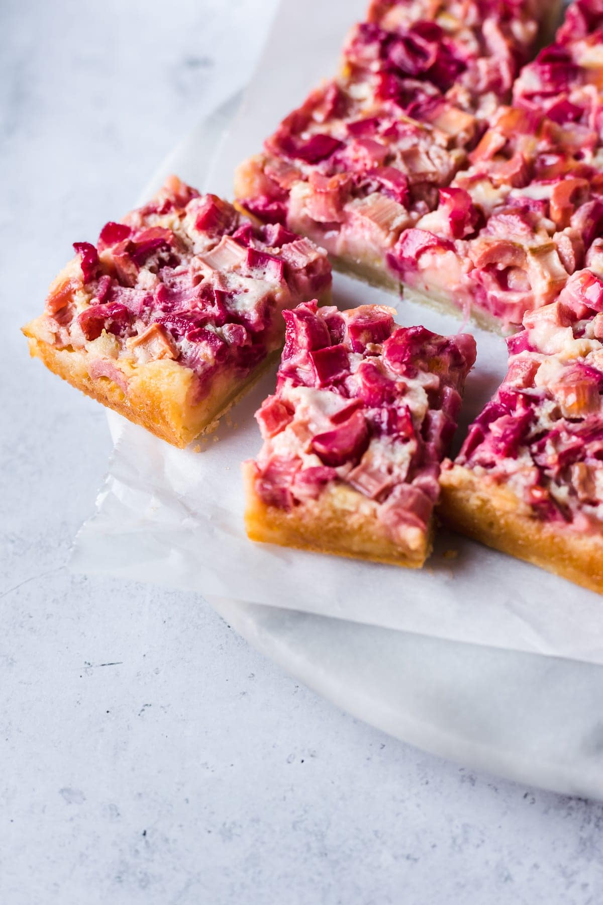 Slices of rhubarb bars on white parchment and a white marble platter