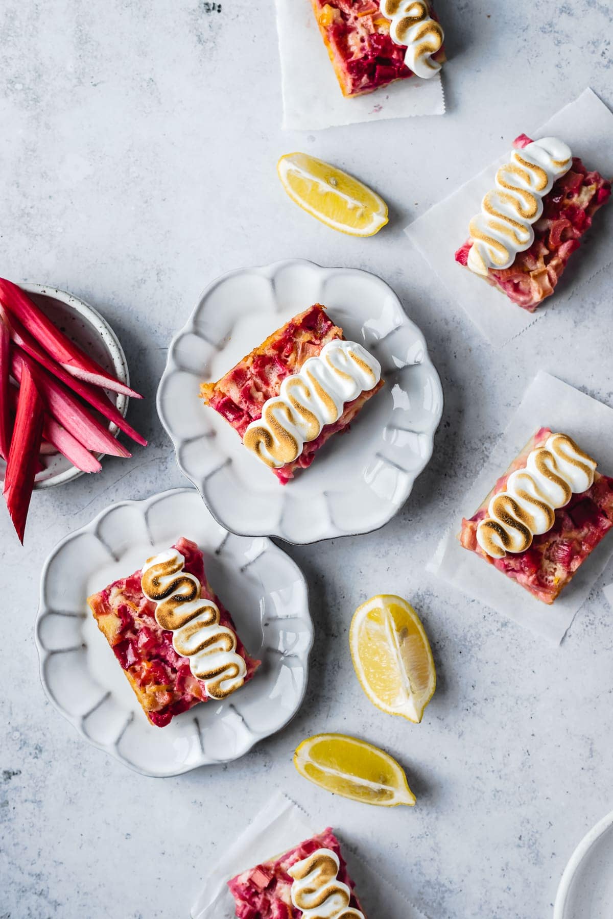 Bar cookies with decorative meringue piping on plates and parchment squares on a white concrete surface