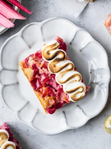 Lemon rhubarb bar on a white plate and white cement surface with lemons and rhubarb nearby