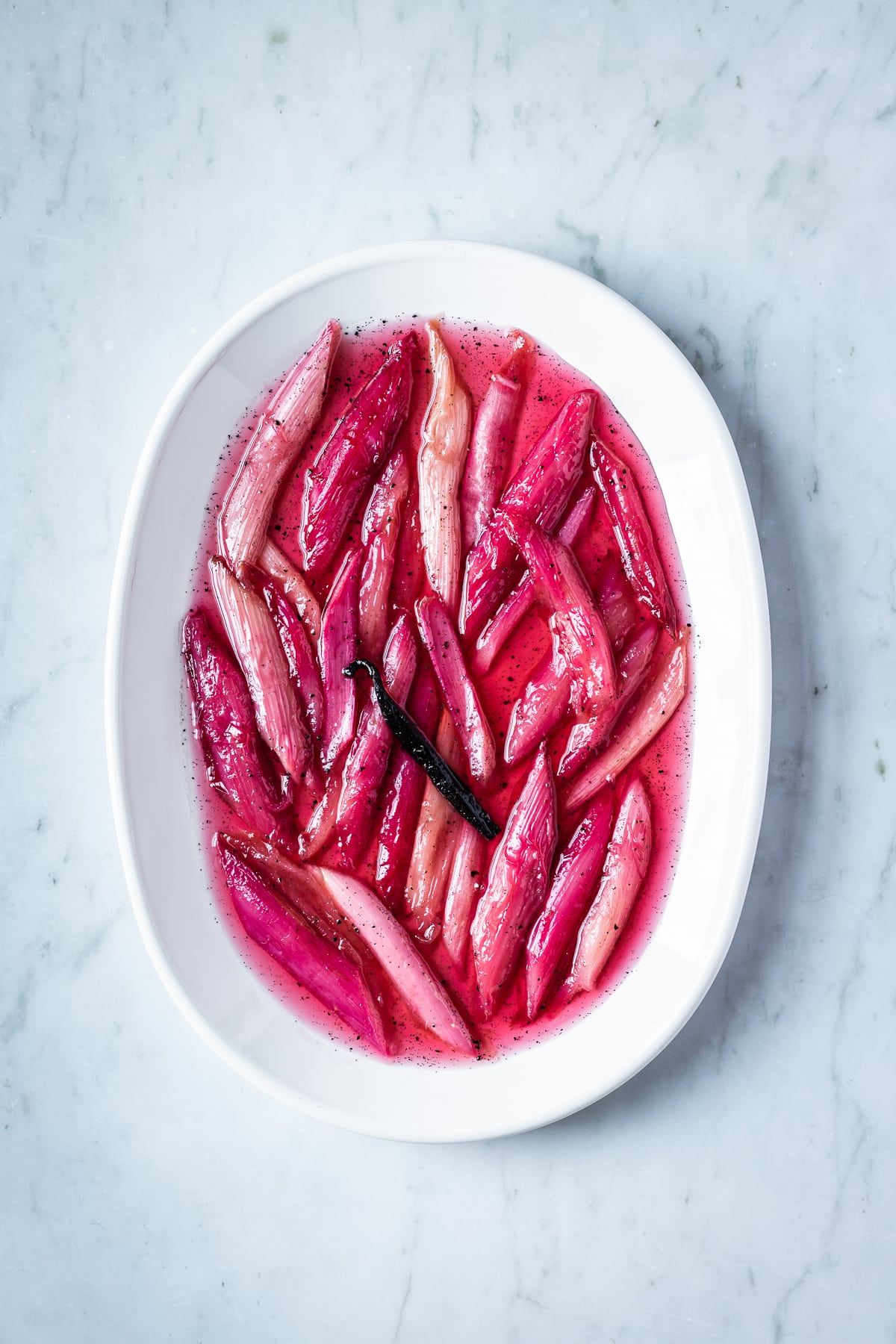 Bright pink poached rhubarb on a white oval platter on a grey marble surface