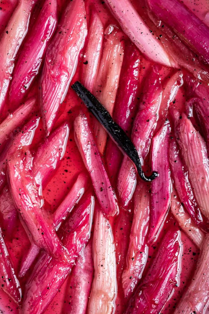 Close up of bright pink poached rhubarb with black pepper, cardamom and vanilla pod