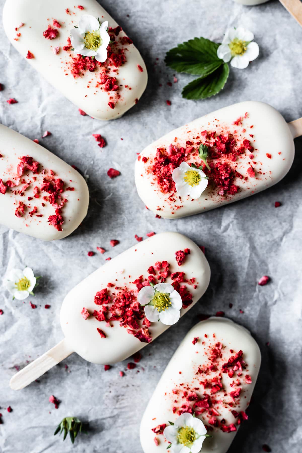 Five ice cream bars on white parchment paper. There are strawberry blossoms on four of the bars.