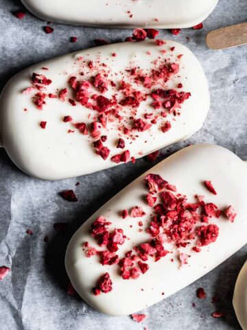 Closeup of strawberry rhubarb ice cream bars covered in white chocolate with freeze dried strawberry bits sprinkled on top