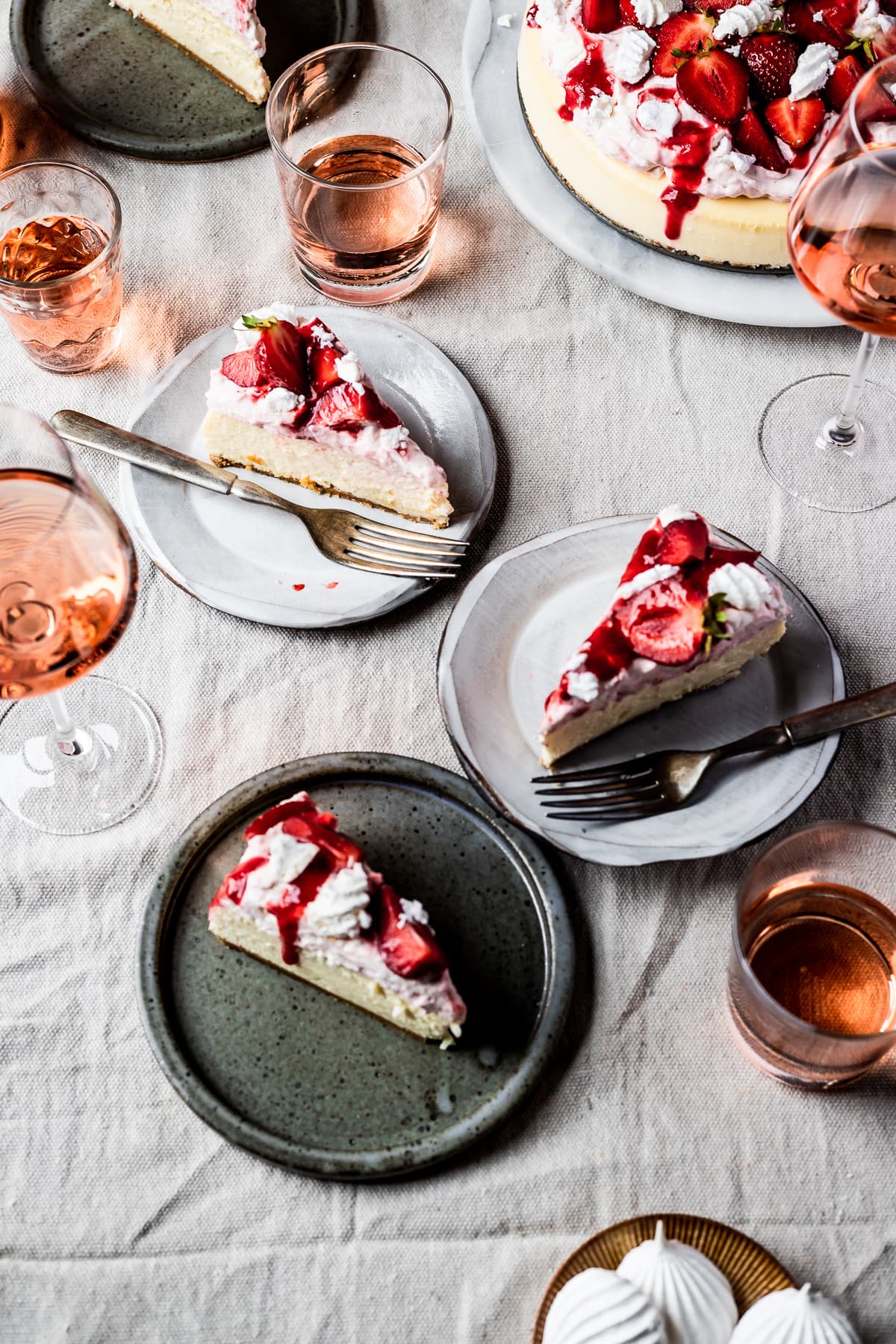 A picnic scene with slices of cheesecake on plates on a linen cloth with glasses of rosé wine nearby.