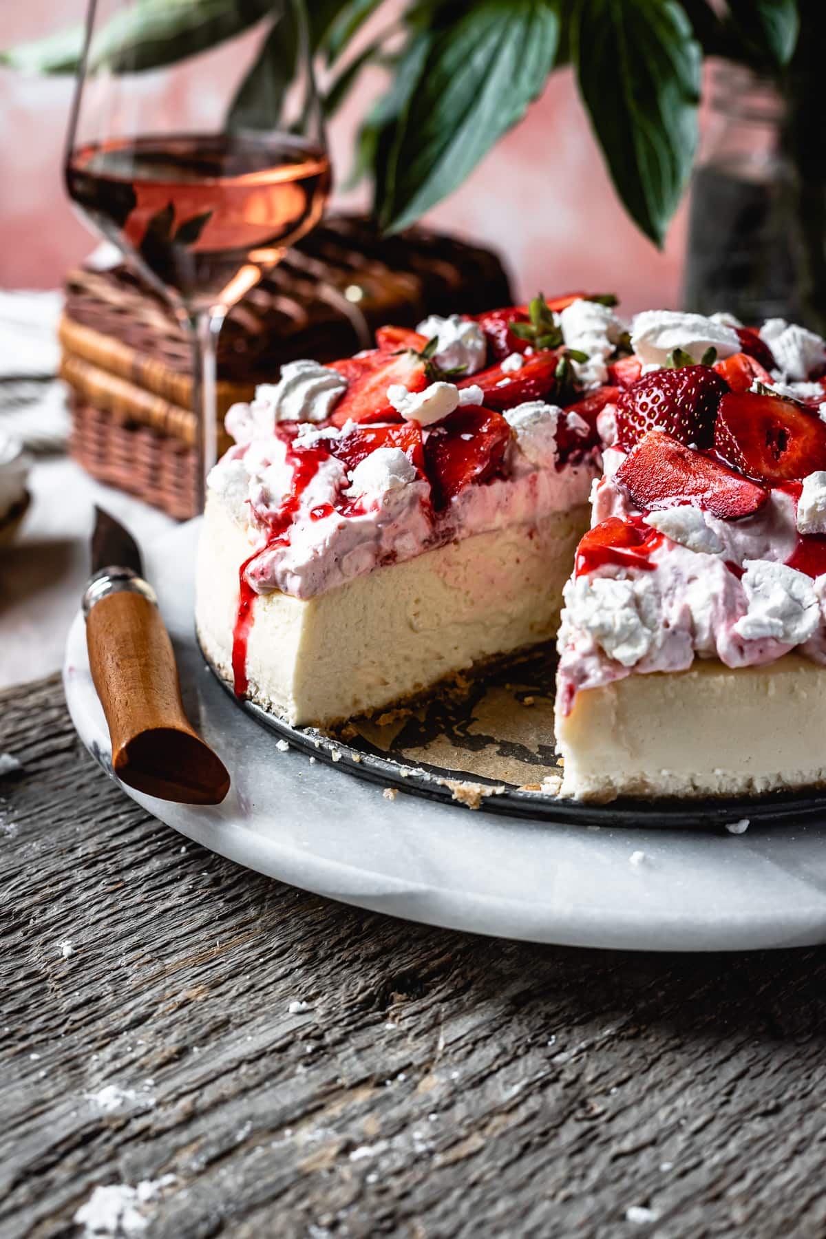 Side view of cheesecake with a slice cut out of it, revealing the creamy interior. The cheesecake is topped with whipped cream, strawberries and meringues.