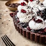 A chocolate cherry tart with whipped cream and chocolate shavings.