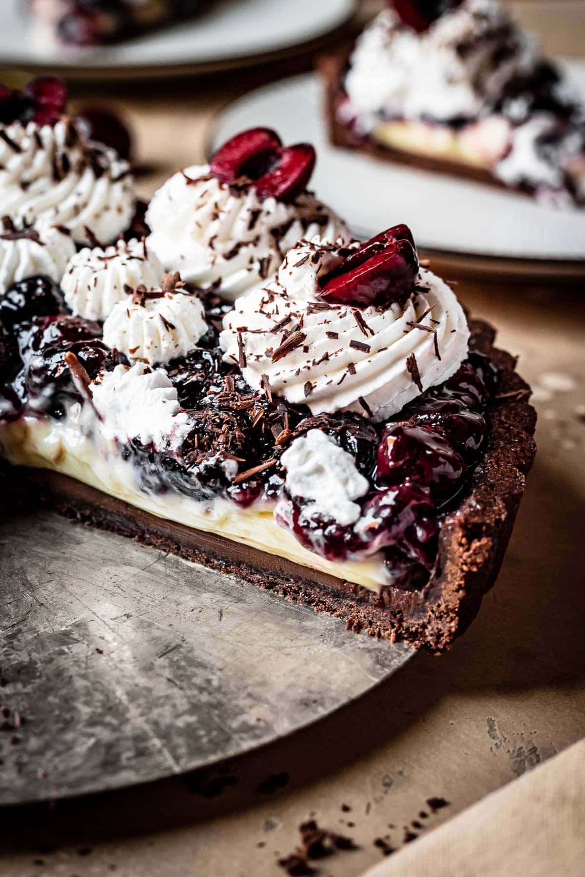 A close up side view of the sliced interior of a fruit and pastry cream tart, with whipped cream piping and cherries on top.