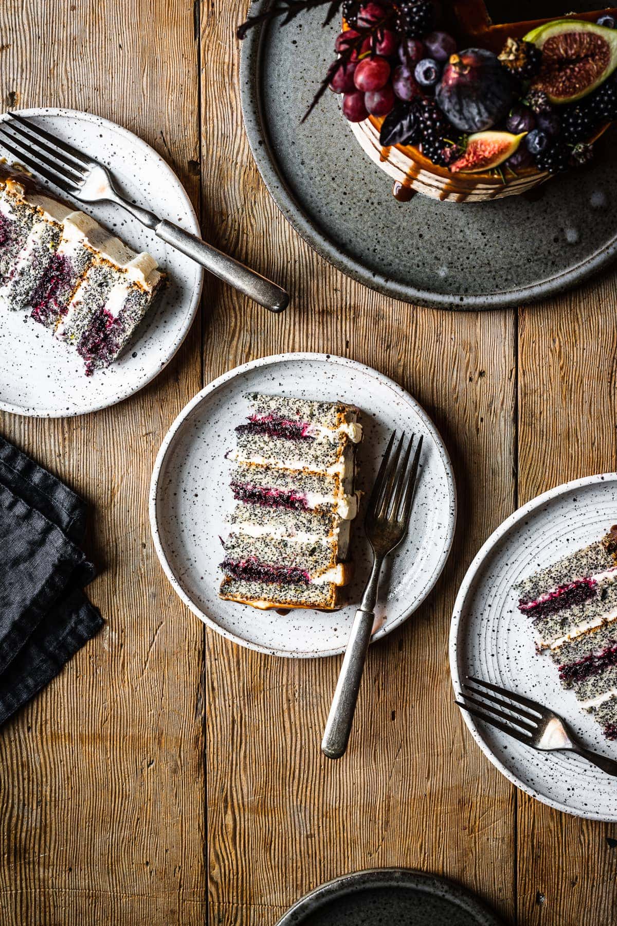 Three slices of blackberry poppy seed cake on white ceramic plates.