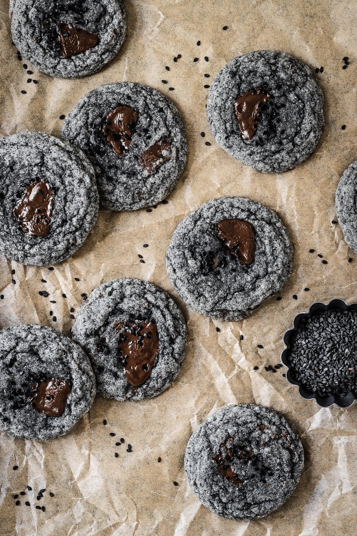 Black sesame cookies with pools of melted chocolate on a brown parchment paper background.