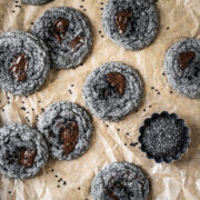 Black sesame cookies with pools of melted chocolate on a brown parchment paper background.