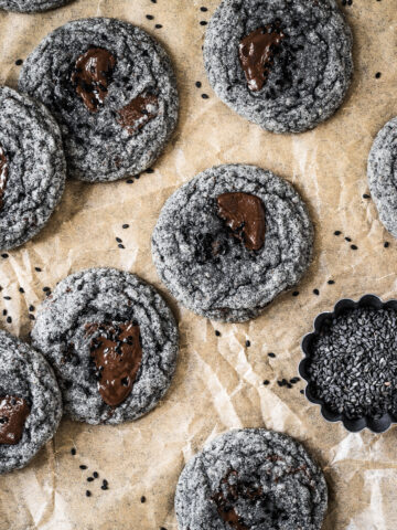 Black sesame cookies with pools of melted chocolate on a brown parchment paper background.