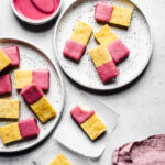 Cornmeal bars dipped in pink glaze on white plates and white parchment squares